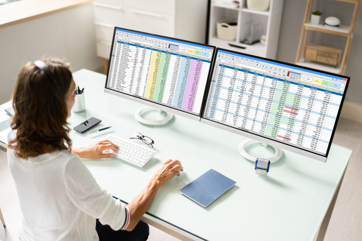 Bookkeeper working with dual monitors displaying spreadsheets for financial reporting and bank reconciliations