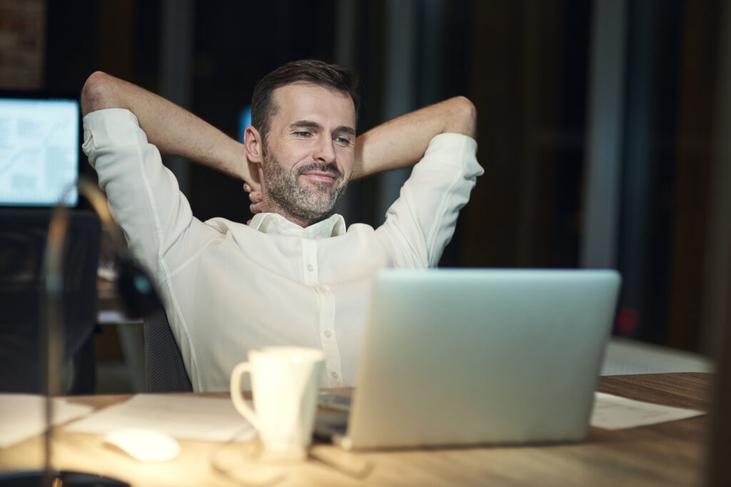 Smiling businessman relaxing at desk after finishing work, showing the benefits of outsourcing data entry and system setup.